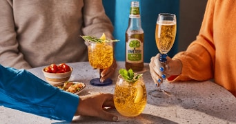 Drie personen proosten met glazen cider aan een tafel, met een fles Somersby Apple cider en hapjes zoals cherrytomaatjes en garnalen in bakjes.