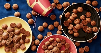Schalen met kruidnoten en pepernoten op een blauwe tafel, met een Sinterklaashoed ter decoratie.