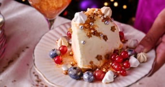 Feestelijke dessert met bessen en meringue op een bord, versierd voor Kerstmis, met een glas sprankelende drank op de achtergrond.