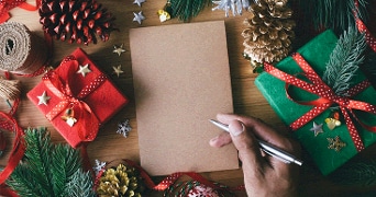 Tafel vol kerstversiering met schrijfblok, hand en pen