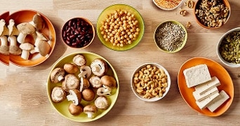 Paddestoelen, tofu, kikkererwten, noten, zaden en peulvruchten op een houten tafel.