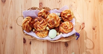 Mandenvlecht gevuld met gevlochten broodjes en een gekleurd ei op een houten tafel.