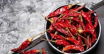 Kom schaaltje met gedroogde rode pepers op grijze achtergrond