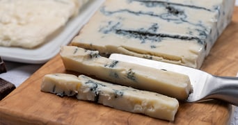 Stukken blauwaderkaas op een houten plank met kaasschaaf