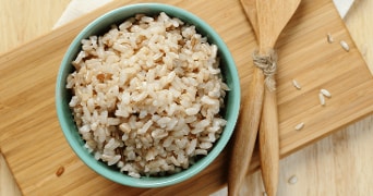 Schaaltje bruine rijst op een houten snijplank met houten lepels.