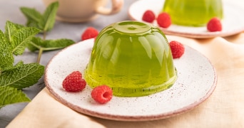Groene gelatine dessert op een bord met verse frambozen en muntblaadjes.