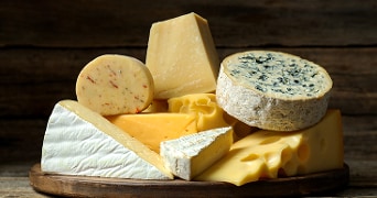 Verschillende soorten kaas op een houten plank, waaronder brie, blauwaderkaas, gatenkaas en harde kazen.