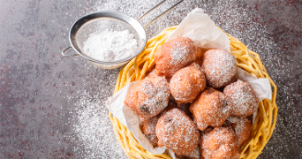 Oliebollen in een mandje met poedersuiker erover gestrooid en een zeefje met poedersuiker ernaast