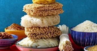 Verschillende soorten ongekookte noedels en rijst op kleurrijke borden en kommen.