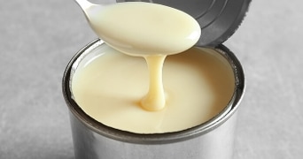 Geopende blik gecondenseerde melk met een lepel die de melk uitschept