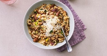 Risotto met groenten en Parmezaanse kaas in een kom, met geraspte kaas geserveerd in een klein bakje.