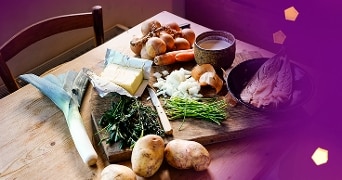 Ingrediënten voor een herfstmaaltijd met prei, aardappelen, uien, kruiden, wortel, botervisfilet en melk op een houten tafel.