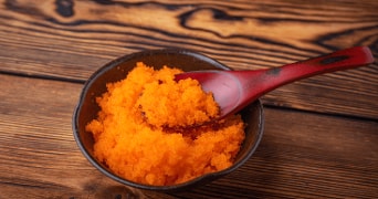 Oranje viskuit in een donker schaaltje met een roodbruine lepel, op een houten ondergrond