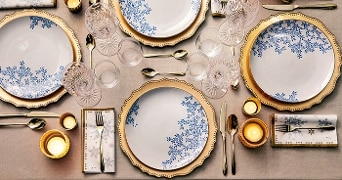 Stijlvol gedekte tafel met elegant servies met blauwe bloemenmotieven en gouden randen, omringd door glazen en bestek.
