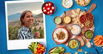 Plank met diverse dips en hapjes zoals hummus, groenten en crackers.