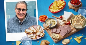 Diverse borrelplank met verschillende soorten kaas, worst en dips, vergezeld van tortillachips, worteltjes en tomaatjes.