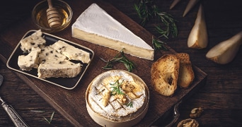 Borrelplank met verschillende soorten kaas, toast, walnoten, takjes rozemarijn en partjes peer op een houten plank