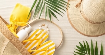Strandaccessoires met gele slippers, zonnebril en strohoed op zand achtergrond.