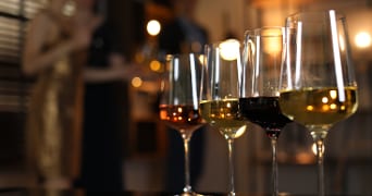 Wijnproeverij met verschillende glazen witte, rode en rosé wijn op tafel, op de achtergrond mensen in feestkleding