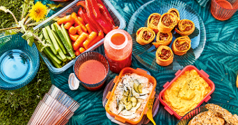 Picknick opstelling met groentesnacks, dipsauzen en wraps op een kleed.