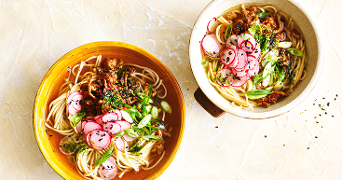 Twee kommen ramen met gesneden radijs, lente-ui, groenten en kruidige toppings.