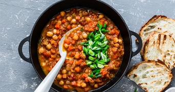 Stoofpot van kikkererwten met tomaat en lente-uitjes geserveerd met gegrild brood