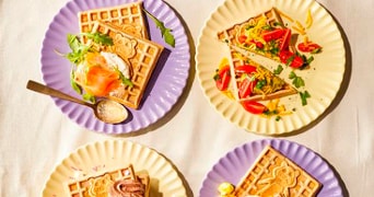Vier borden met verschillende soorten wafels, elk belegd met diverse toppings zoals zalm, roomkaas, groenten, chocolade en ei.