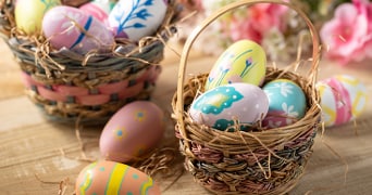 Paasmandjes gevuld met kleurrijk versierde paaseieren op een houten tafel, omringd door bloemen