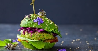 Vegetarische burger met groene broodjes, verse slablaadjes, paarse kool, eetbare bloemen en sesamzaadjes als garnering