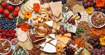 Luxe kaasplank met verschillende soorten kaas, crackers, druiven, verse bessen, noten, gedroogd fruit en honing, feestelijk gegarneerd met eetbare bloemen.