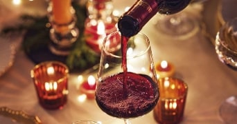 Rode wijn wordt in een glas geschonken op een feestelijk gedekte tafel met kaarslicht