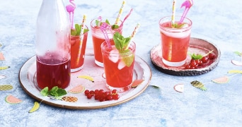 Rode cocktails met ijsblokjes en munt, geserveerd in glazen met flamingo-rietjes en een fles ernaast op een dienblad.