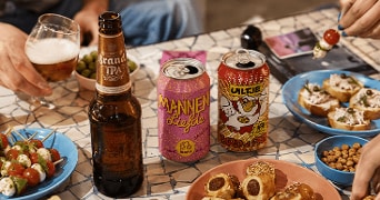 Bierfles en twee bierblikjes van de merken Brand, Mannenliefde en Uiltje op een tafel met verschillende hapjes zoals caprese spiesjes, gevulde toastjes, saucijzenbroodjes en olijven.