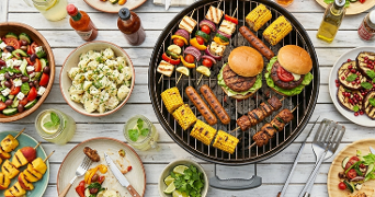Barbecue scène met diverse gerechten: hamburgers, grillworst, maïskolven, groentespiesjes en verschillende salades rondom een barbecuegrill.