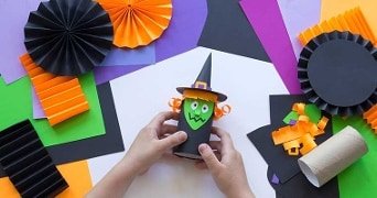 Halloween-knutselwerk met een papieren heksfiguur en kleurrijke vouwblaadjes.