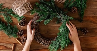 Kerstkrans maken met dennentakken, dennenappels en touw op houten tafel