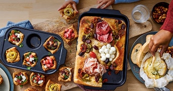 Verschillende pizza- en gebakvariaties met toppings zoals tomaat, mozzarella, carne en olijven, verdeeld over een houten tafel.
