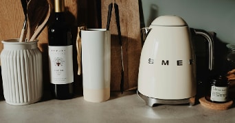 Keukenblad met SMEG waterkoker, fles rode wijn, houten lepels in een witte houder en een kaars.