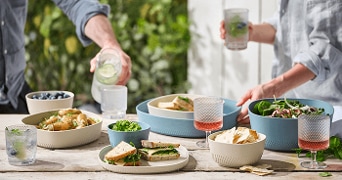 Tafel gedekt met diverse gerechten en glazen drank tijdens een buitenlunch met twee mensen.