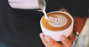 Koffie met latte art in een witte kop, geschonken door een barista.