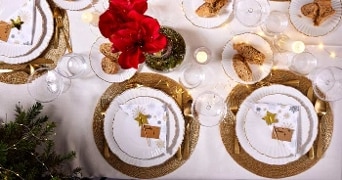 Feestelijke gedekte tafel met gouden bestek, kerstdecoratie en rode bloemen.