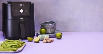 Digitale airfryer met Blue logo, limoen, gember en sperziebonen op een paarse tafel.