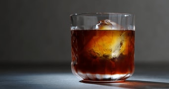 Glas met een donkerbruine cocktail en een groot ijsblokje