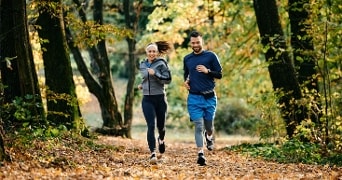 Twee mensen hardlopend op een bospad omringd door herfstbladeren