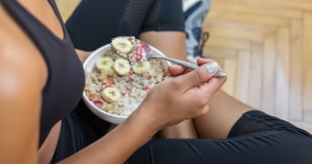 Persoon eet een kom havermout met banaan en fruit.