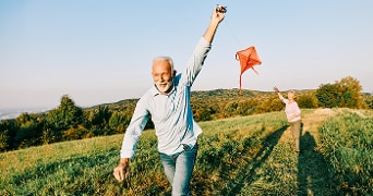 Twee mensen die met een vlieger in een groen landschap spelen.