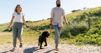 Een koppel wandelt met hun hond langs een pad in een groen graslandschap.
