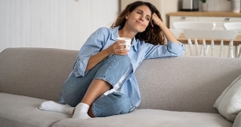 Vrouw zit ontspannen op een bank en houdt een mok vast in een lichte woonkamer
