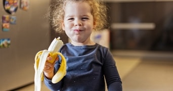 Kind met een gepelde banaan in de hand in een keuken