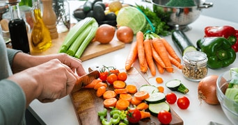 Verse groenten worden gesneden op een snijplank, waaronder wortels, komkommer, cherrytomaatjes en paprika's.
